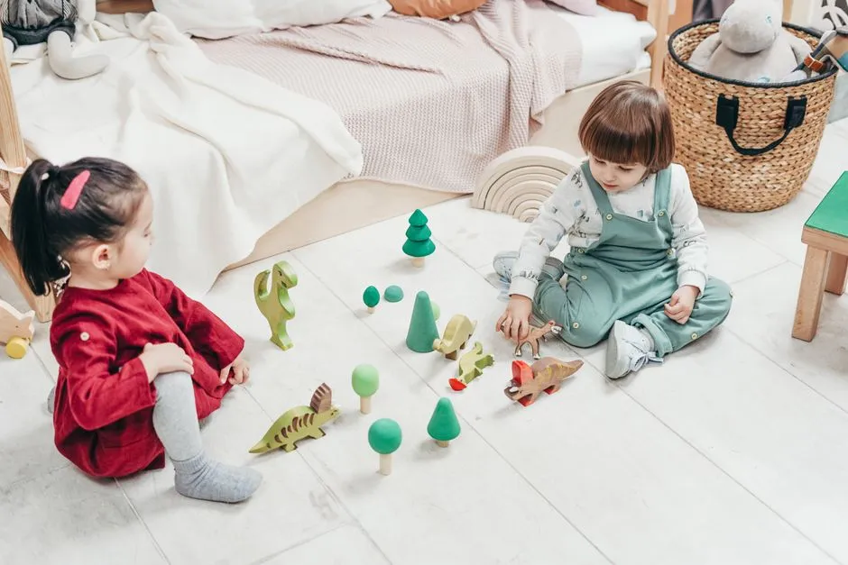Two toddlers sitting on a bedroom floor playing with wooden toy blocks and figures
